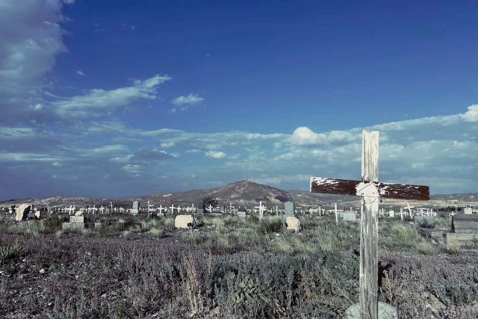 Old cemetery with weathered wooden cross grave markers in Goldfield, Nevada with mountain in background and blue sky.